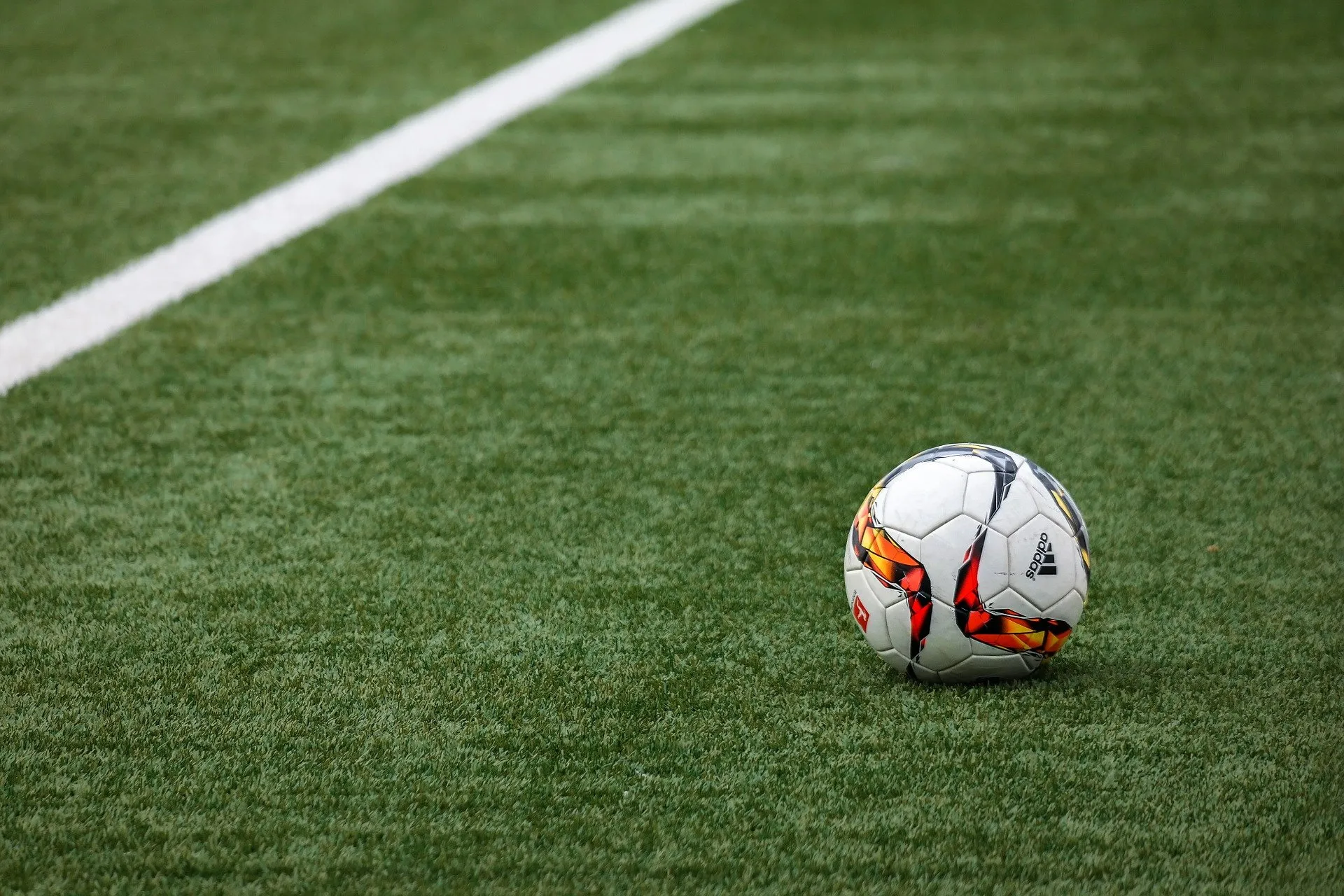 A soccer ball with a white, red, and black pattern rests on a green artificial grass field in El Mirage near a crisp white boundary line—showcasing quality artificial turf installation.